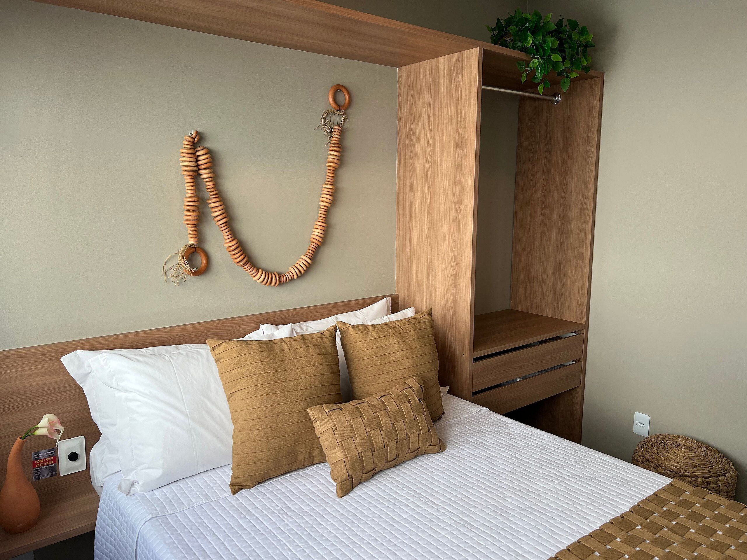 Ein ordentlich bezogenes Bett mit weißer und brauner Bettwäsche, einem hölzernen Kopfteil und einer an der Wand befestigten Holzleiste mit Schmuck.