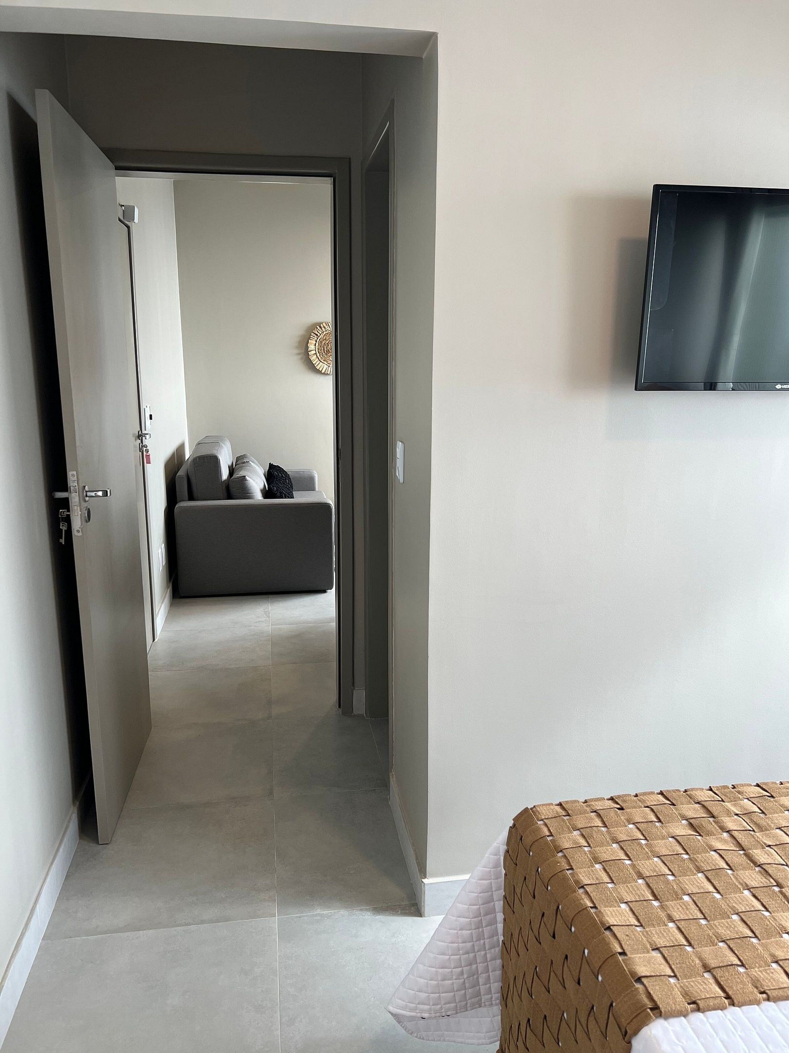 Habitación de hotel con cama, televisor montado en la pared y puerta que da a otra habitación.