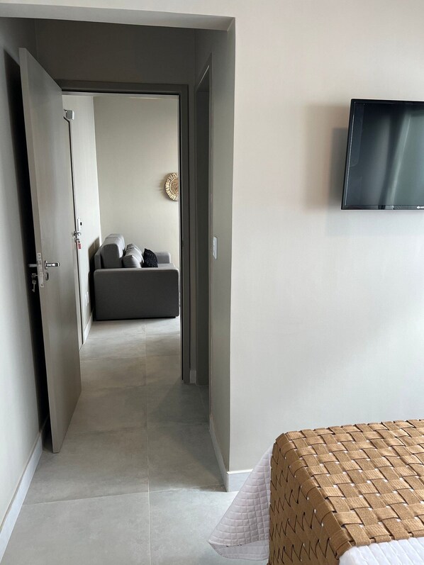 A hotel room with a bed, a TV mounted on the wall, and a door leading to another room. - MAR DOS CORAIS (Maceió)