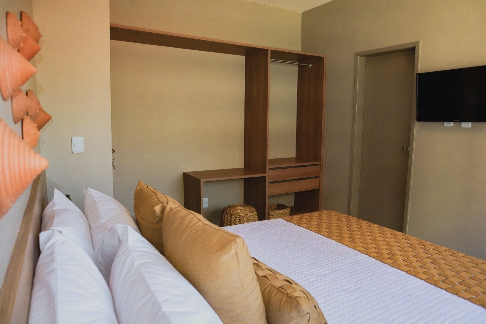 A hotel room with a bed, a wardrobe, a television, and a wall-mounted shelf.