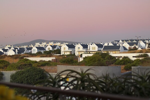 A row of modern houses with uniform architecture, a flat roof, and a backdrop of a hill.