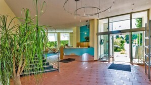 A modern interior with a reception desk, a staircase, and a large potted plant. - Seepark Hotel am Wandlitzsee (Wandlitz)