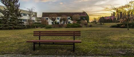 A park with a wooden bench, a grassy field, and a building with a red roof in the background.