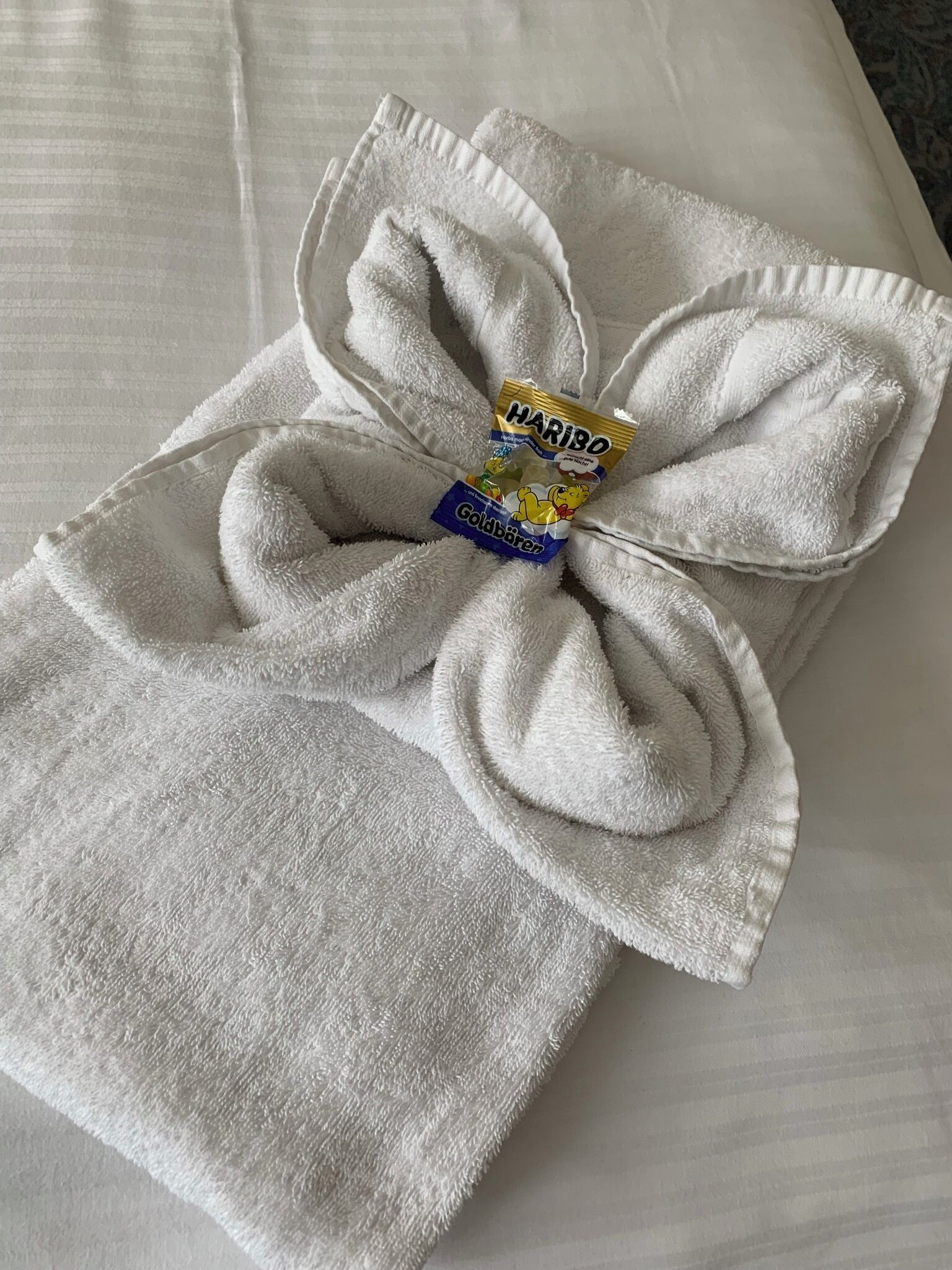 A neatly folded white towel with a Haribo Goldbär package placed on top.