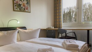A hotel room with two beds, a desk, a chair, a telephone, and a window with a view of trees. - Seepark Hotel am Wandlitzsee (Wandlitz)