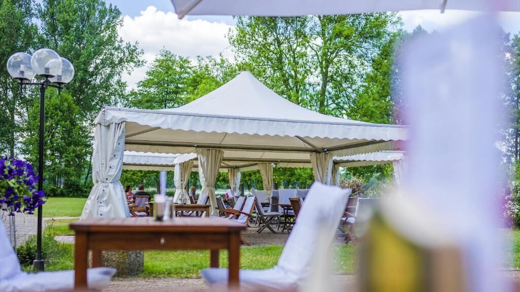 A tented outdoor area with tables and chairs, surrounded by greenery.