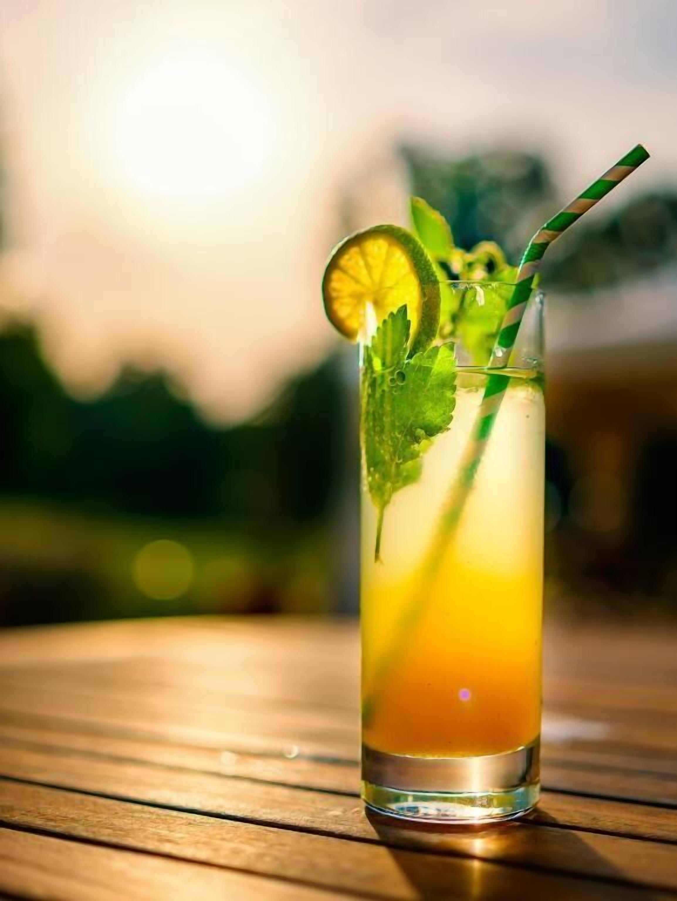 A tall glass with a layered drink, garnished with a lime slice and mint leaves, on a wooden table.