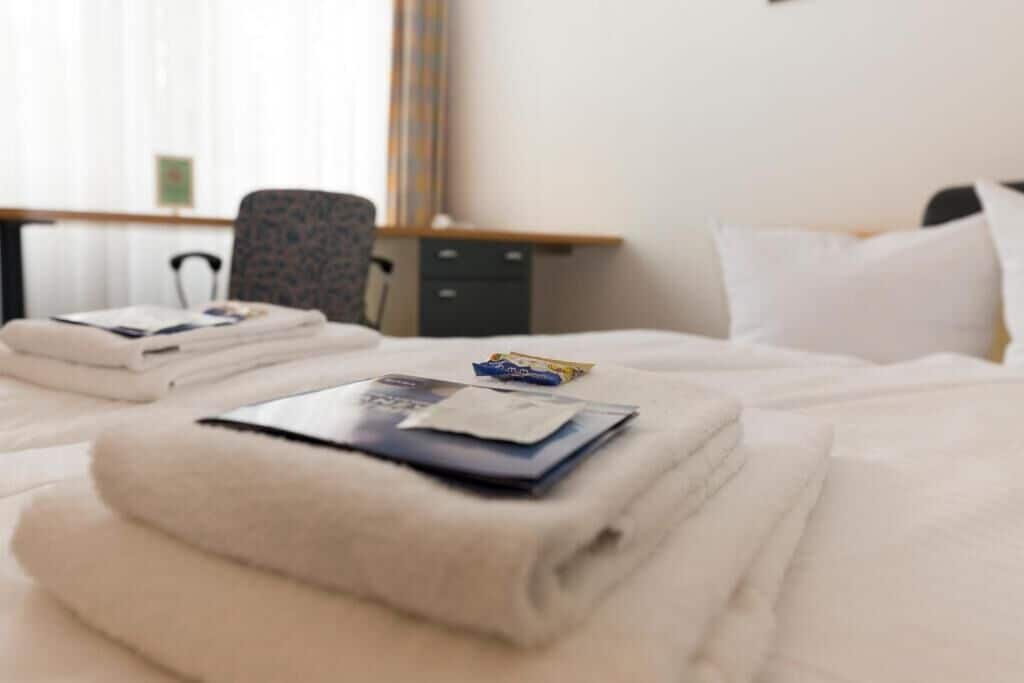 Una cama bien hecha con una toalla blanca doblada, una revista y un objeto pequeño sobre la cama.