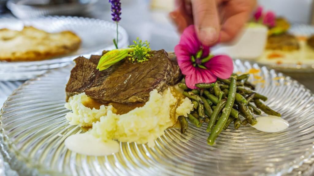 A plate with mashed potatoes, green beans, and a piece of meat garnished with a flower.