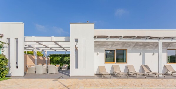 Uma área de piscina moderna ao ar livre, com espreguiçadeiras e um pérgola.
