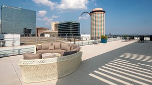 A rooftop lounge with a woven sofa, a view of the city skyline, and a clear sky. - Ballpark Luxury Loft Steps from Arch (St. Louis)