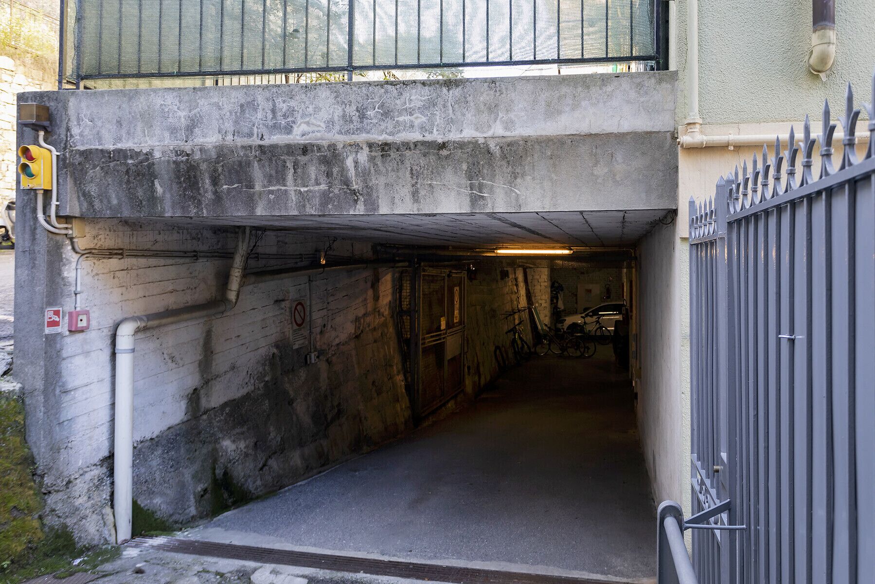A narrow, dimly lit underground passageway with concrete walls, a metal gate, and a bicycle parked inside.