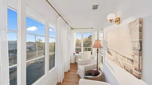 A narrow hallway with large windows, a desk, a chair, and a lamp.