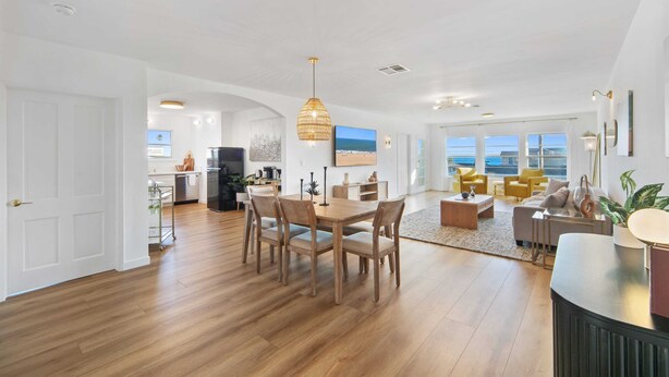 A spacious living area with a wooden dining table, chairs, and a large window offering a view.