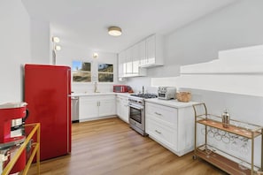 Une cuisine moderne avec des meubles blancs, un réfrigérateur rouge, une cuisinière à gaz et une machine à café.