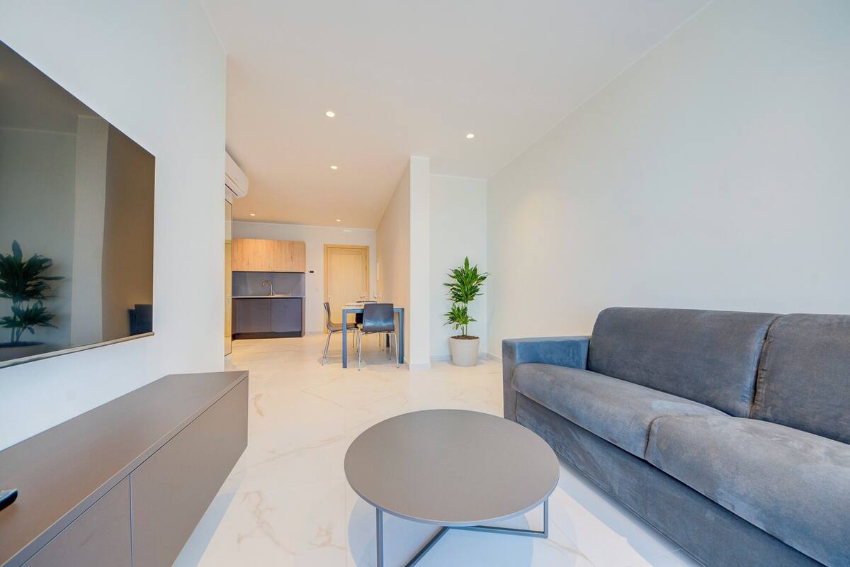 Un salon moderne avec un canapé gris, une petite table ronde et un coin repas comprenant une table et des chaises.