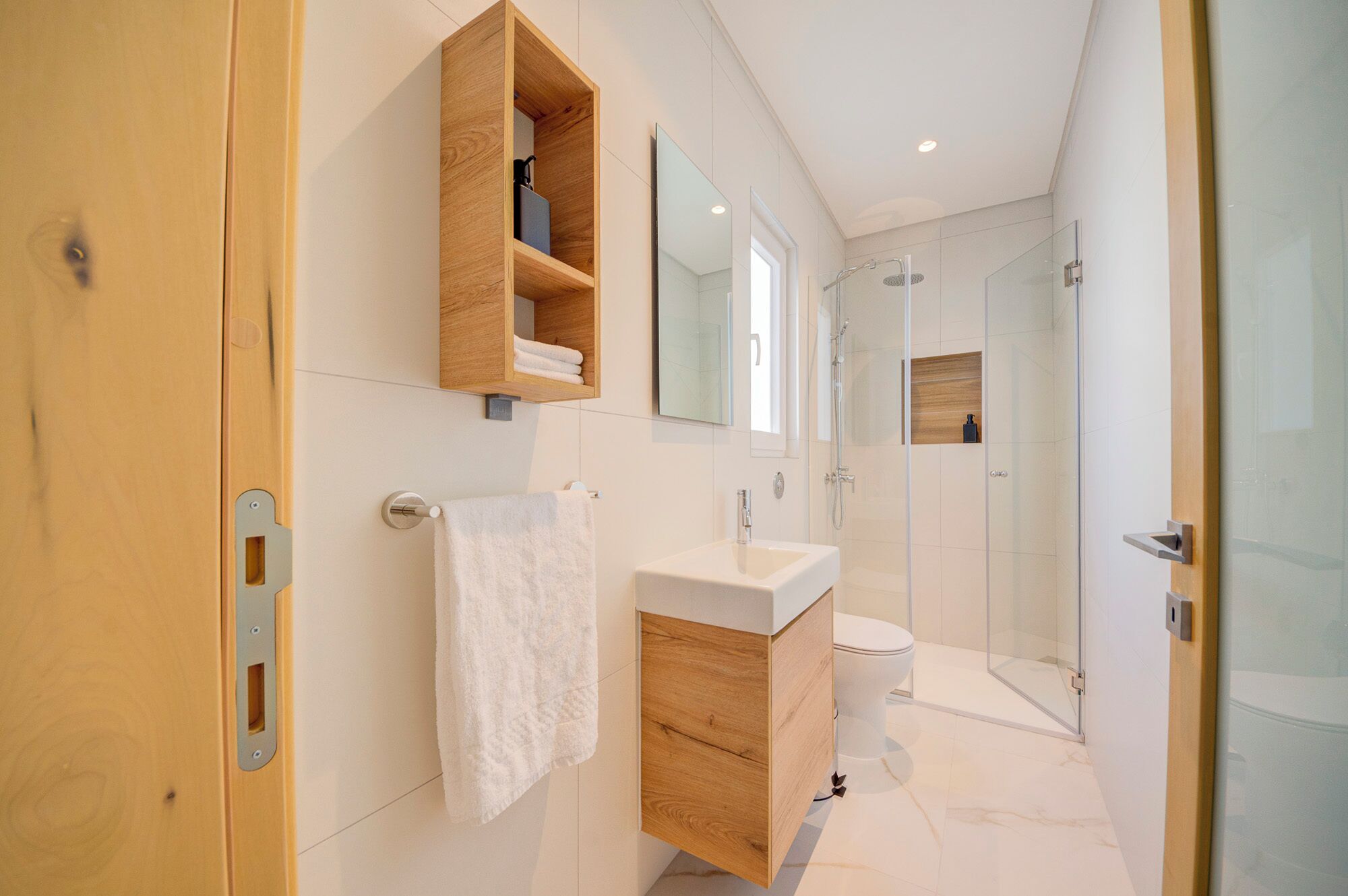A modern bathroom with a wooden vanity, a glass shower enclosure, and a white toilet.