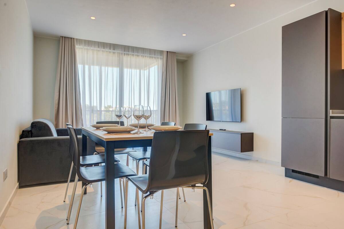 Un espace repas moderne avec une table dressée pour quatre personnes, un canapé et un téléviseur fixé au mur.