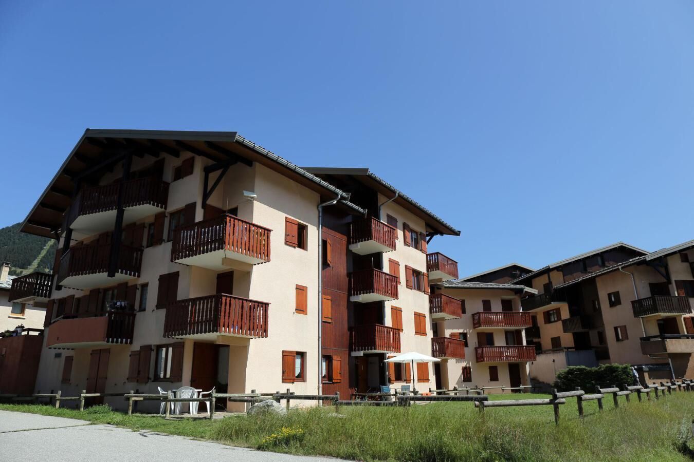 A multi-story building with balconies, a paved area in front, and a clear sky.