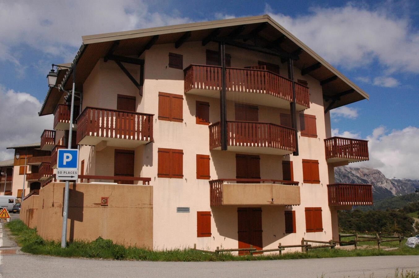 A multi-story building with balconies, a parking sign, and a mountainous backdrop.