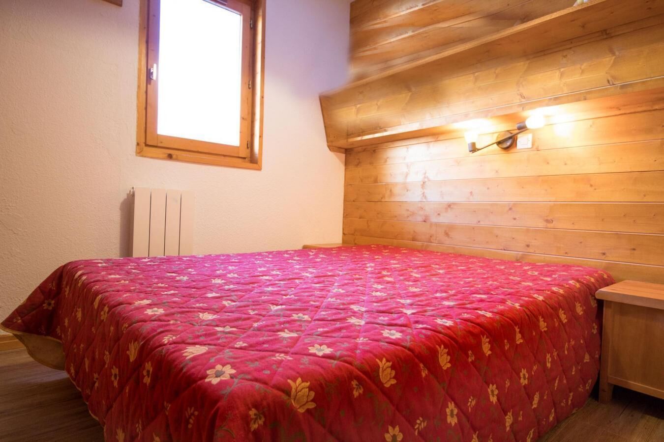 A bedroom with a wooden headboard, a window, and a bed with a floral bedspread.