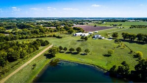 An aerial view of a rural property with a large field, a pond, and several buildings including a barn and a house.