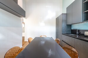 A modern kitchen with a dark countertop, a built-in oven, and a sink. There are four chairs with a woven design around a rectangular table. - Loft Porta Maggiore - Three Bedroom Apartment, Sleeps 6 (Rome)