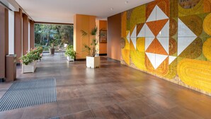 Un hall d’entrée spacieux, avec un mur orné d’un motif décoratif, des plantes en pot et une vue sur l’extérieur.