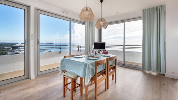 Un coin repas avec une table dressée pour quatre personnes, de grandes fenêtres et une vue sur la mer.