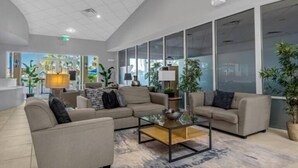 Un hall d’entrée spacieux au design moderne, doté d’un grand espace salon avec des canapés et une table basse, le tout entouré de grandes fenêtres offrant une vue sur l’extérieur.