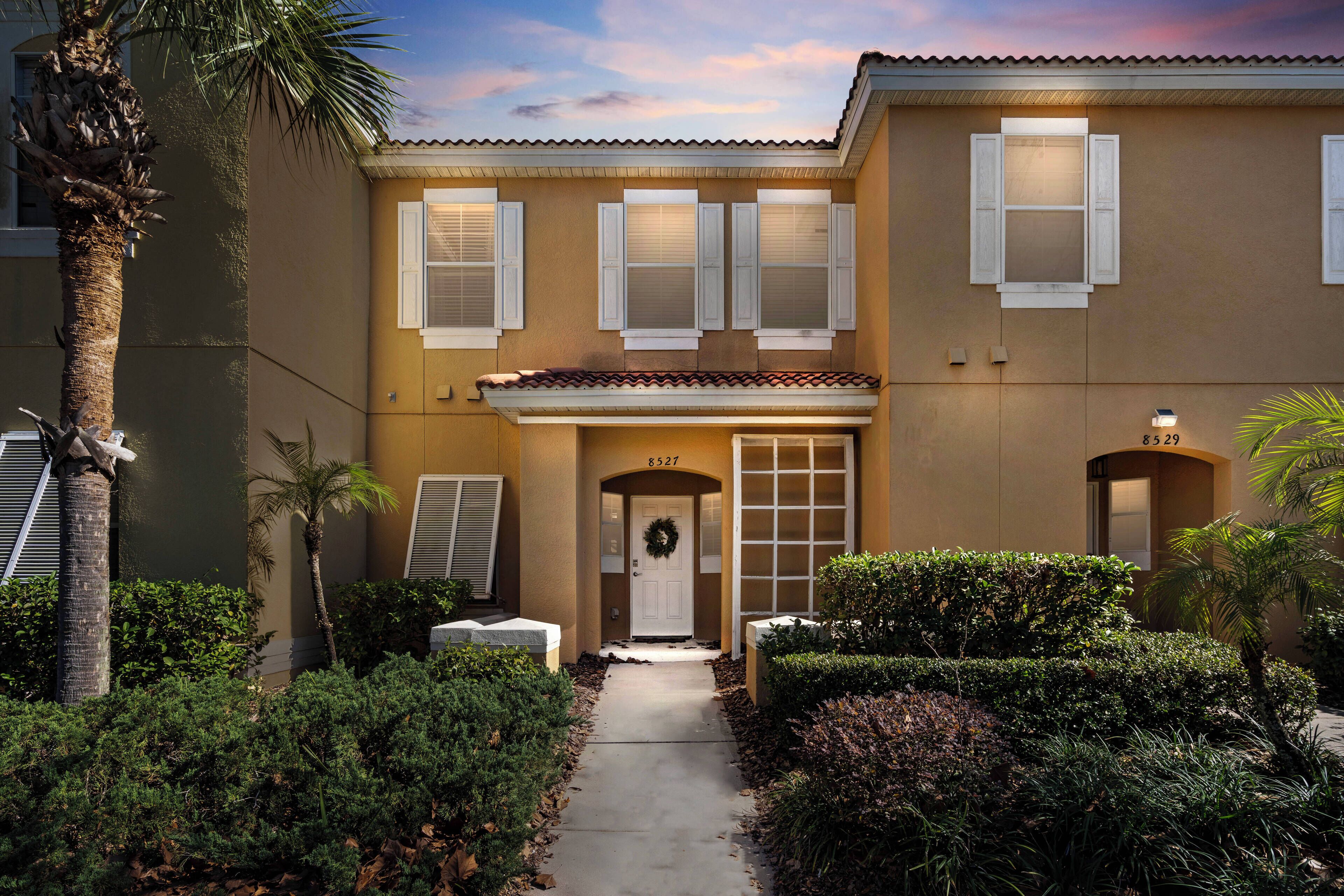 A two-story building with a beige facade, white shutters, and a number 8527 on the door.