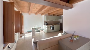 Une cuisine moderne avec des poutres en bois, un coin repas avec une table et des chaises, et un salon avec un canapé et une table basse.