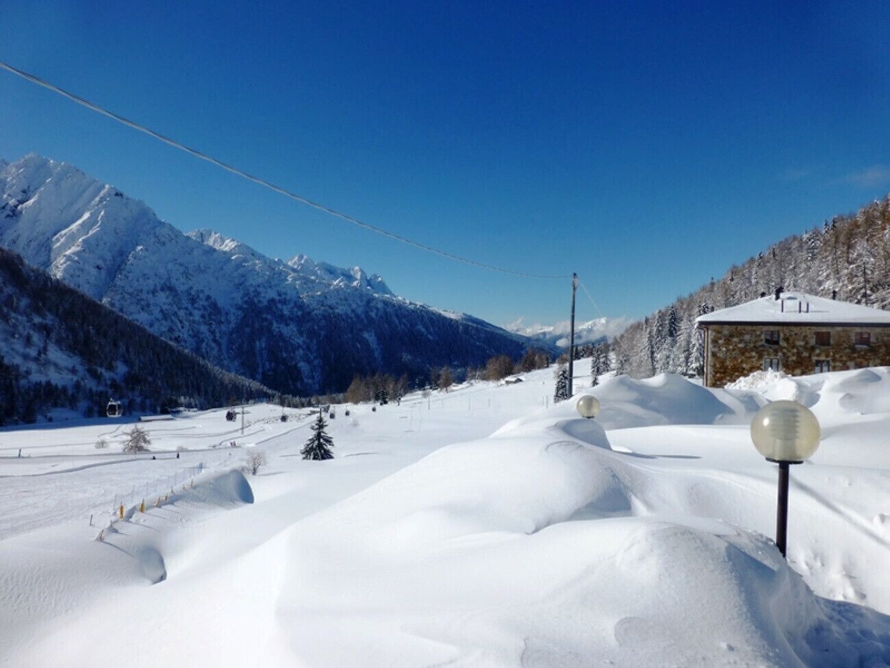 Schneebedeckte Landschaft mit einem Gebäude, blauem Himmel und Bergen im Hintergrund.