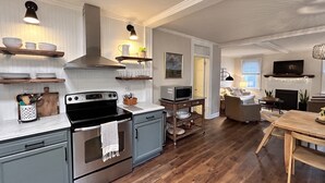 A modern kitchen with stainless steel appliances, wooden shelves, and a dining area with a wooden table and chairs.