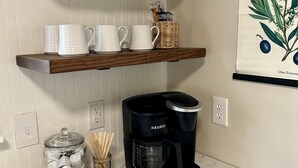 A kitchen counter with a coffee maker, tea pots, and a jar of utensils.