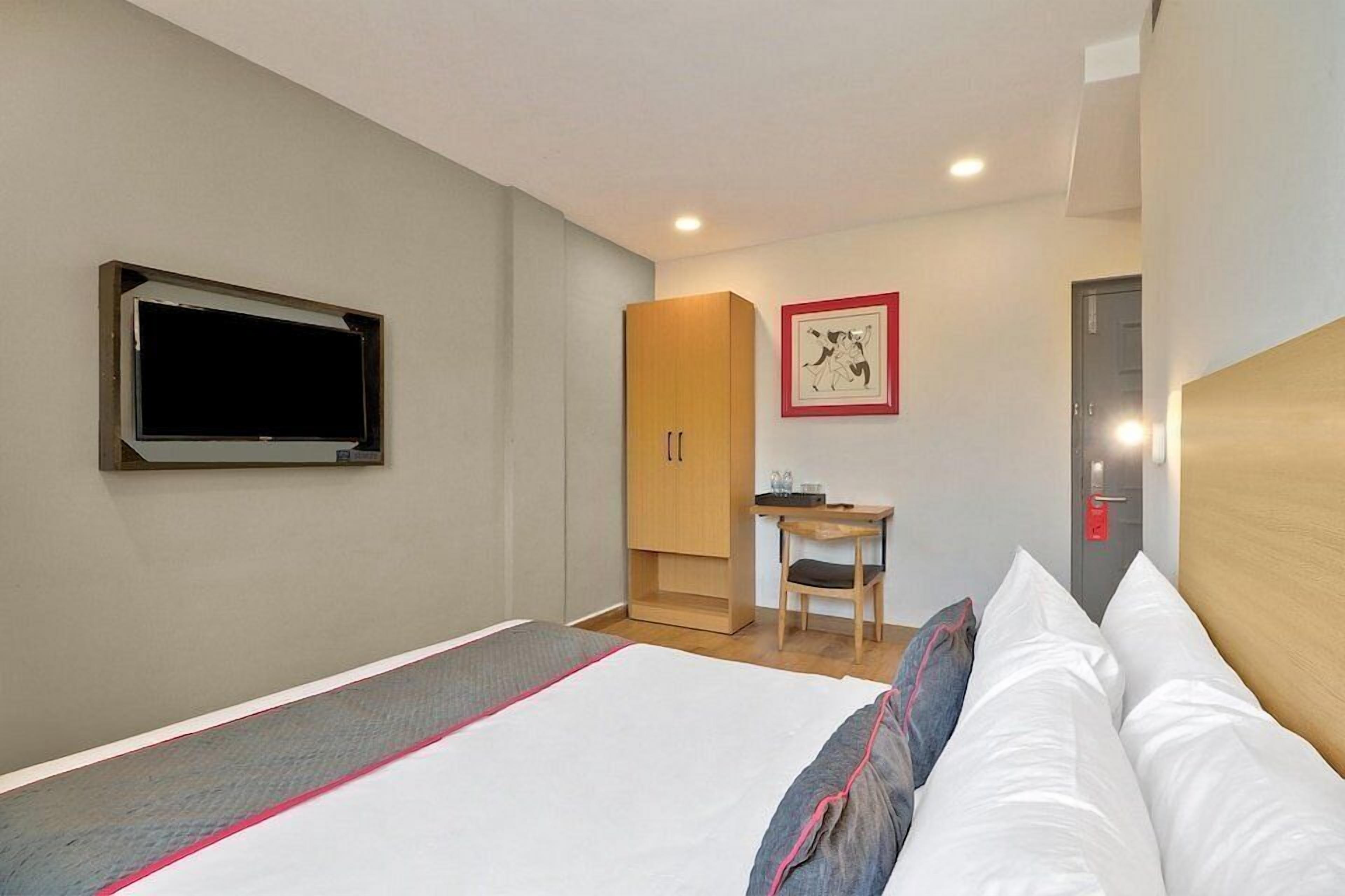 Habitación de hotel con cama, escritorio, armario y un cuadro en la pared.