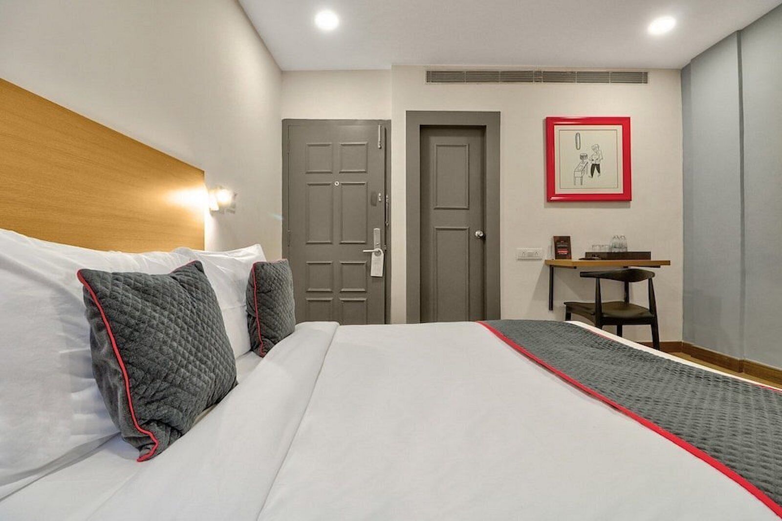 Ein Hotelzimmer mit einem Bett, zwei Türen, einem Schreibtisch und einem gerahmten Bild an der Wand.