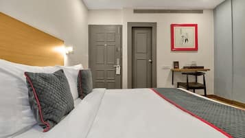 Ein Hotelzimmer mit einem Bett, zwei Türen, einem Schreibtisch und einem gerahmten Bild an der Wand.