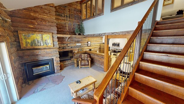 A log cabin interior with a fireplace, a dining area, a kitchen, and a wooden staircase. - Rustic Retreat - Mt Crested Butte (Crested Butte)
