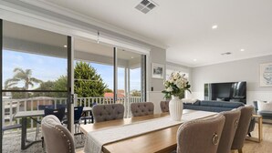 Un salon moderne avec une table à manger en bois, des chaises à revêtement gris, un vase blanc avec des fleurs, un canapé bleu et un téléviseur.