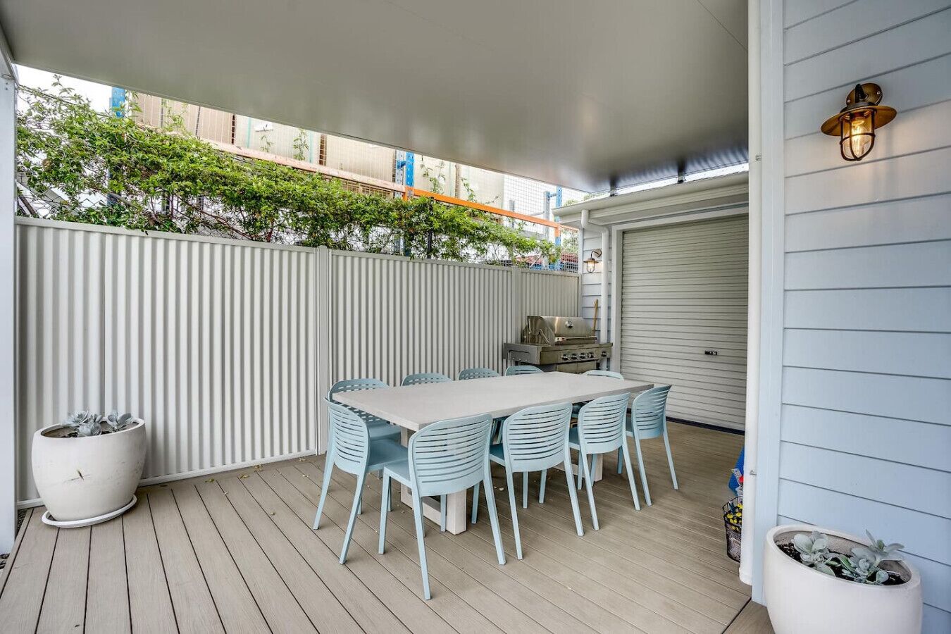 An outdoor patio with a table and chairs, a grill, and potted plants.