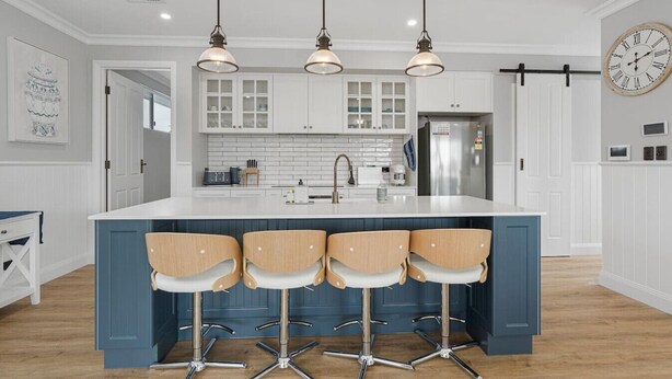 Une cuisine dotée d’un îlot central, de tabourets de bar, de luminaires suspendus et d’une horloge au mur.