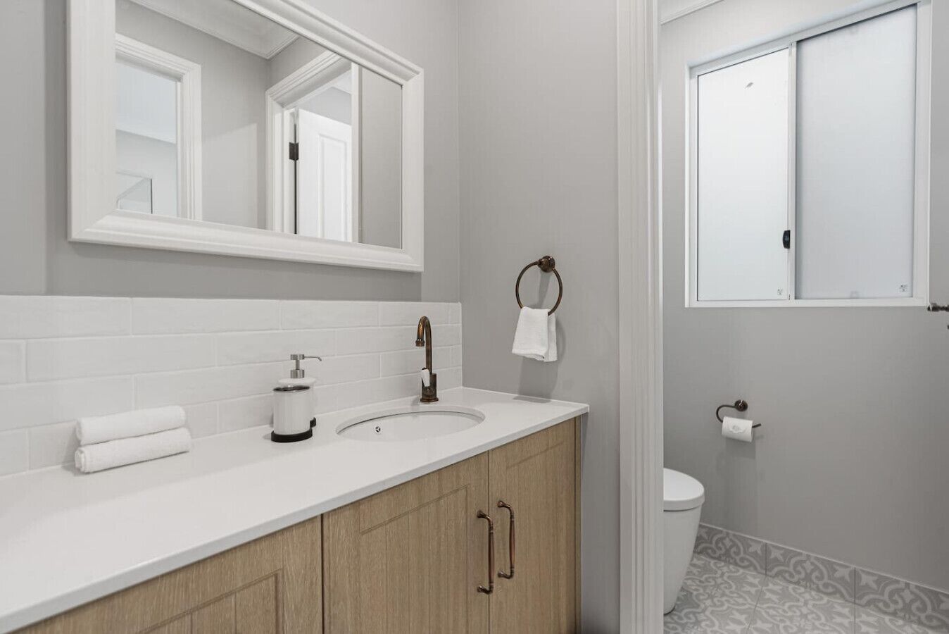 A modern bathroom with a white vanity, a large mirror, a towel rack, and a toilet.