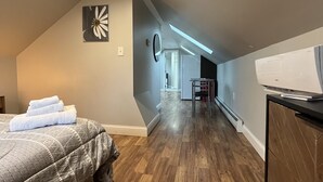 A bedroom with a bed, a desk, and a chair. There is a skylight and a door leading to another room. - Cute & Cozy Providence Studio! (Providence)