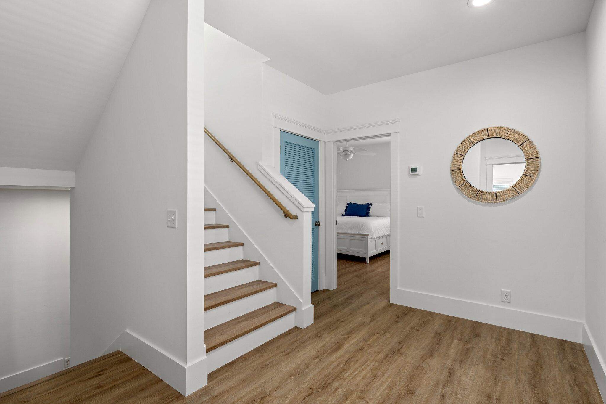 Una escalera conduce a un dormitorio con una puerta azul, un espejo redondo en la pared y suelo de madera.
