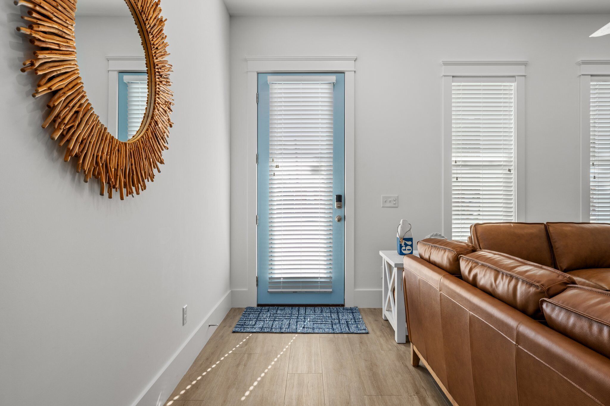 A modern living room with a brown leather sofa, a blue-framed door, and a unique wooden mirror.