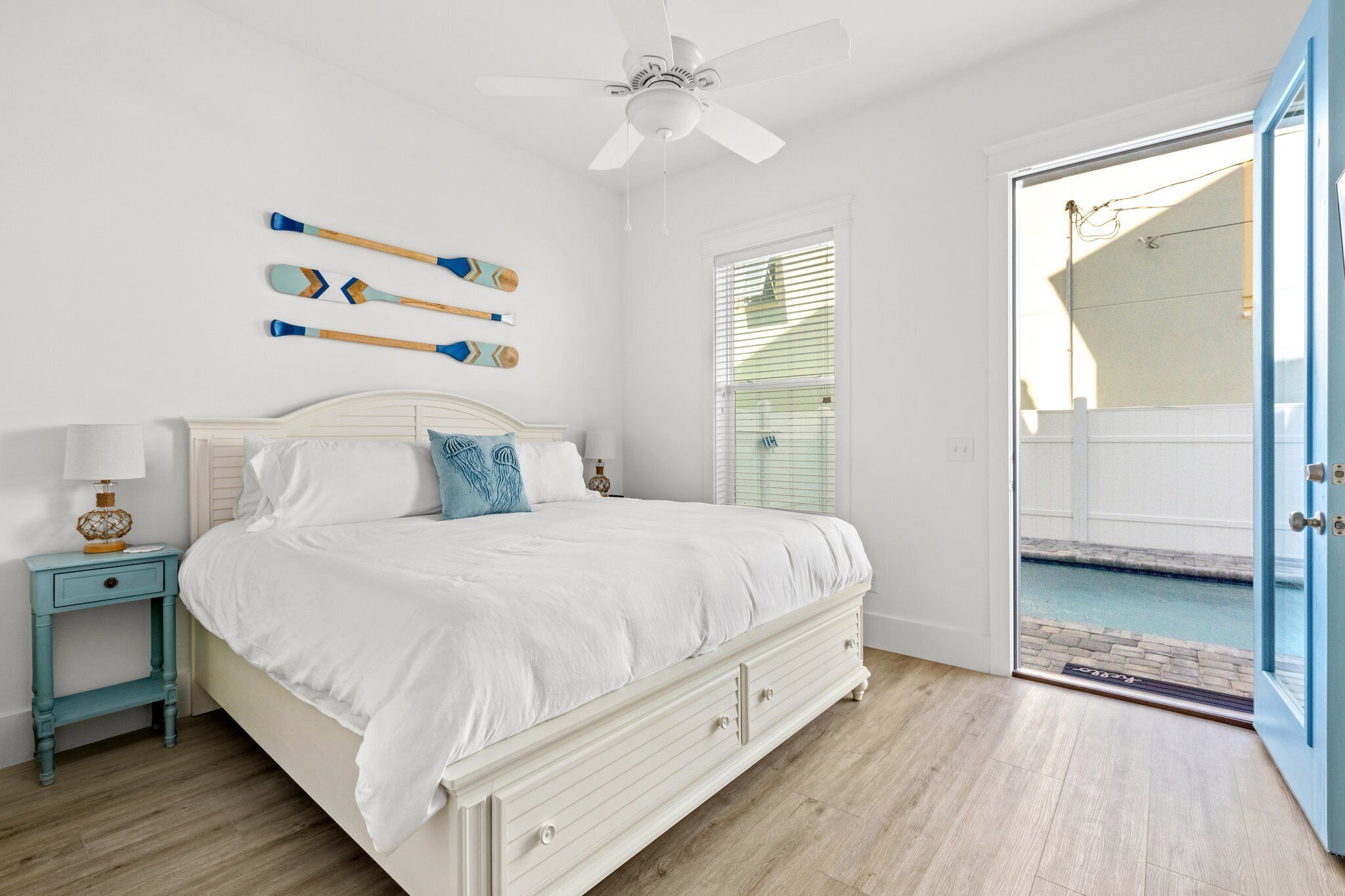 A bedroom with a bed, a nightstand, a ceiling fan, and a view of a swimming pool through an open door.