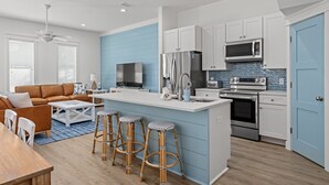 A modern kitchen with white cabinets, stainless steel appliances, and a blue accent wall. - Spectacular 3br 4ba w/ Private Pool, 2 Min Walk to Beach - Sleeps 15! (Panama City Beach)