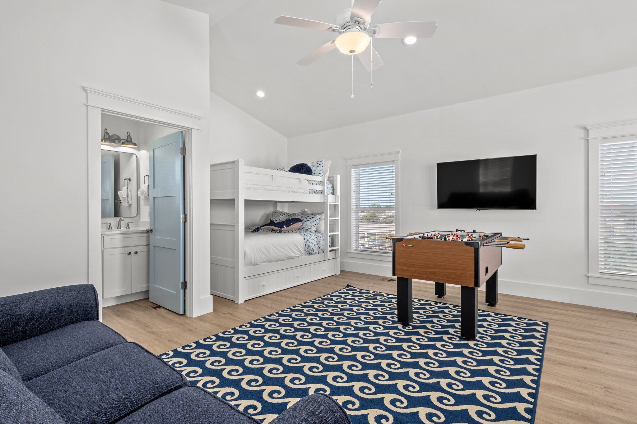 A room with a bunk bed, a foosball table, a TV, and a ceiling fan.