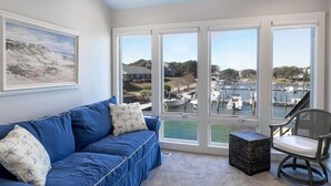 Ein Wohnzimmer mit einem blauen Sofa, einem Sessel und einem großen Fenster mit Blick auf einen Yachthafen.